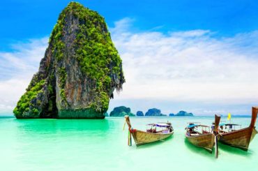 Farallones de piedra caliza y barcas long-tail en una playa de aguas turquesa en Tailandia