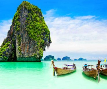 Farallones de piedra caliza y barcas long-tail en una playa de aguas turquesa en Tailandia