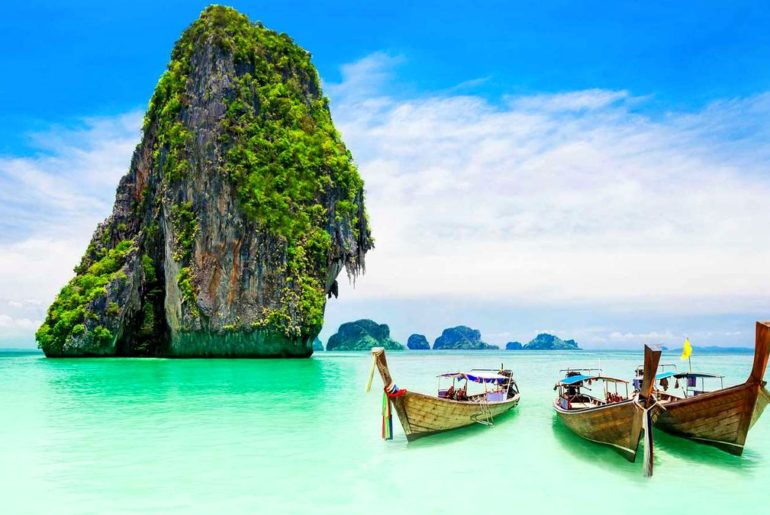 Farallones de piedra caliza y barcas long-tail en una playa de aguas turquesa en Tailandia