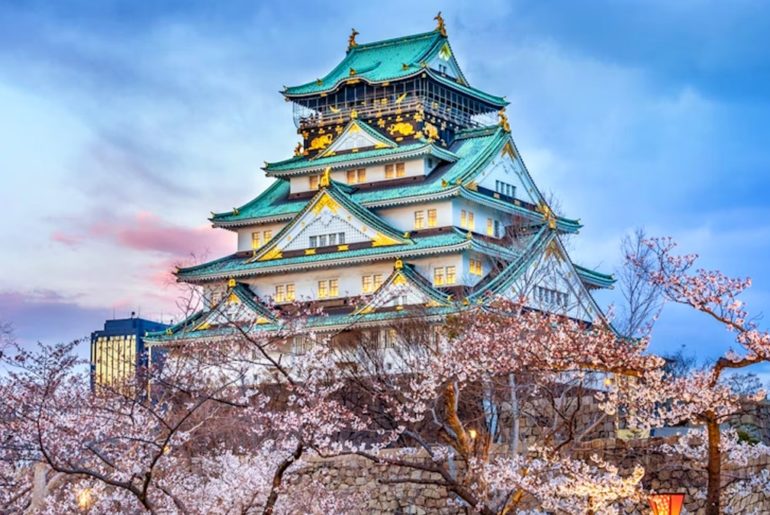 El castillo de Osaka rodeado de cerezos en flor al anochecer