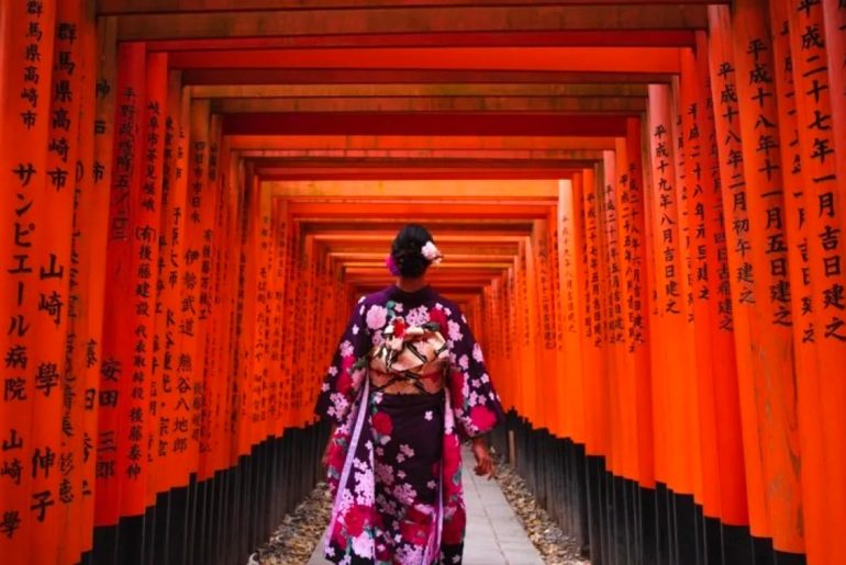 Túnel de puertas torii rojas en Fushimi Inari, Kioto, con una visitante en kimono
